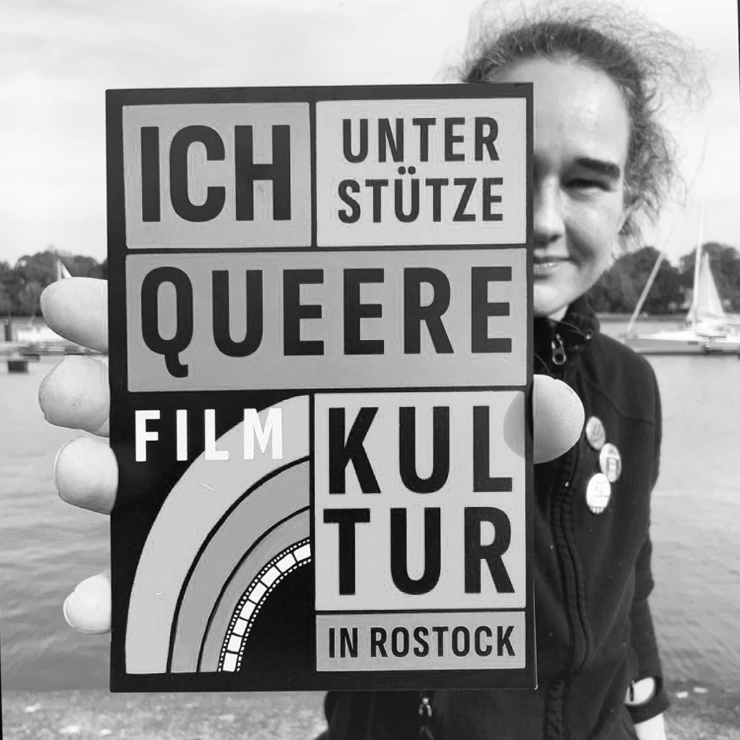 Theresa Brunk hält einen Aufkleber mit dem Text "Ich unterstütze queere Filmkultur in Rostock"
