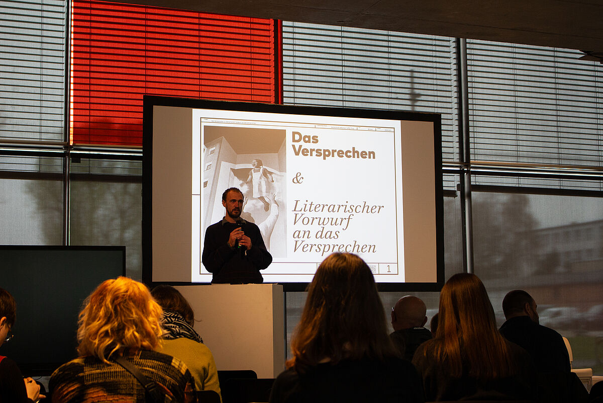 Sally Frey steht auf der Bühne vor einer Leinwand, auf der seine Fotografien zum Thema kulturelle Räume und Teilhabe zu sehen sind.