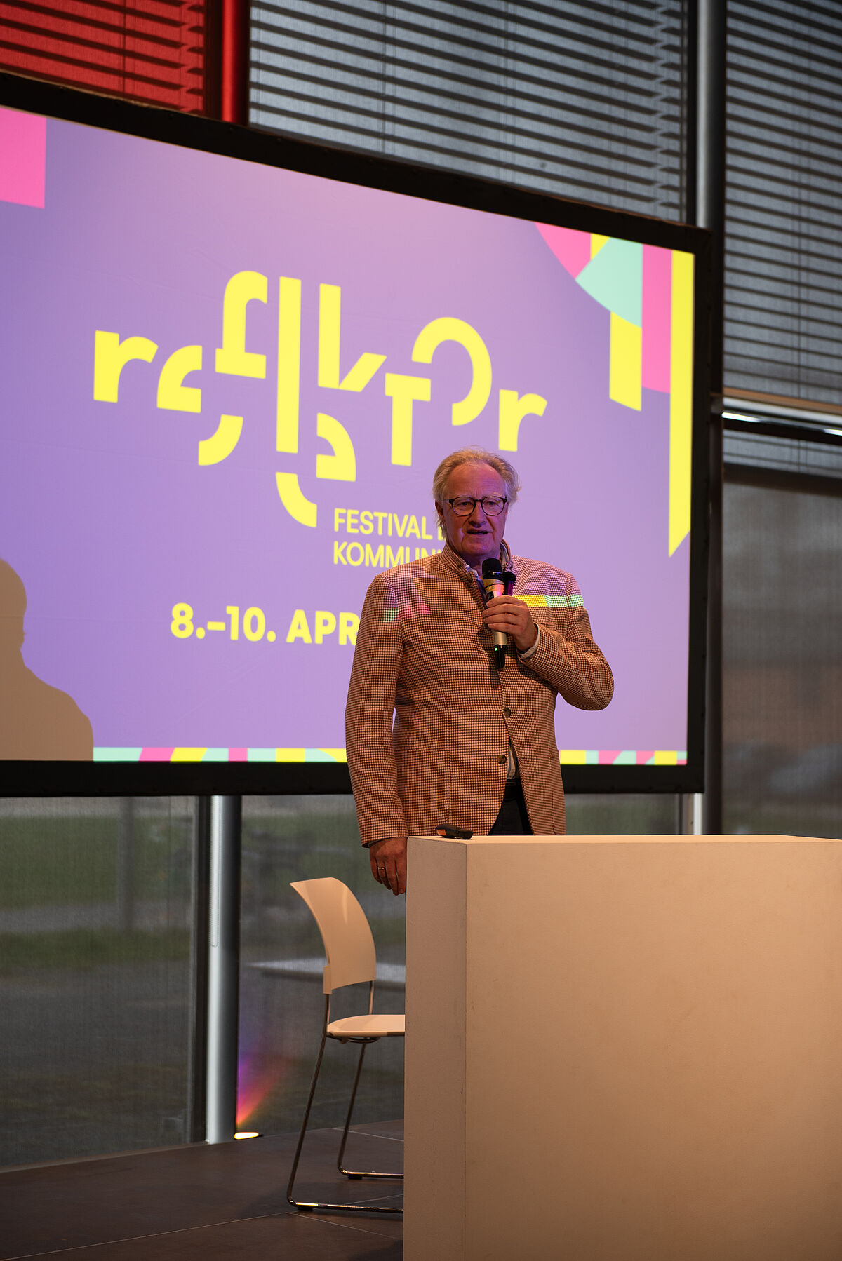 Rektor Bodo Wiegand-Hoffmeister auf der Bühne vor einem Bildschirm auf dem das Reflektor-Logo abgebildet ist.