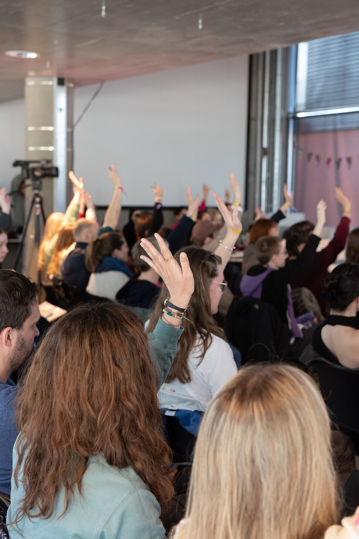 Das Publikum wird von hinten gezeigt, einige Personen heben die Hände, um auf Fragen von Raul Krauthausen während seines Vortrags zu antworten.