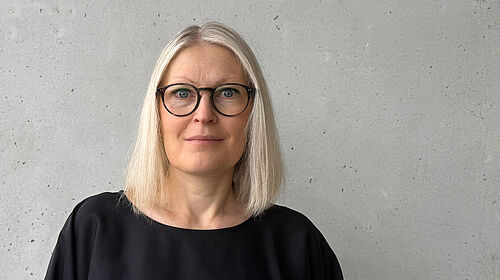 Judith Groß Die Person ist im Porträt vor einer Betonwand zu sehen.