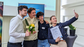 Four young people smile and pose for a selfie, holding flowers and certificates. The three men from the Navoko team and Svea Bublys from the Mjölkav project are celebrating their first and second place wins.