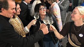 Preisverleihung "one&twenty", die Professoren und Emma Hille stoßen mit Cora Schmidt auf ihren Preis an. Die Professoren und Kommilitonen beglückwünschen Preisträgerin Cora Schmidt.