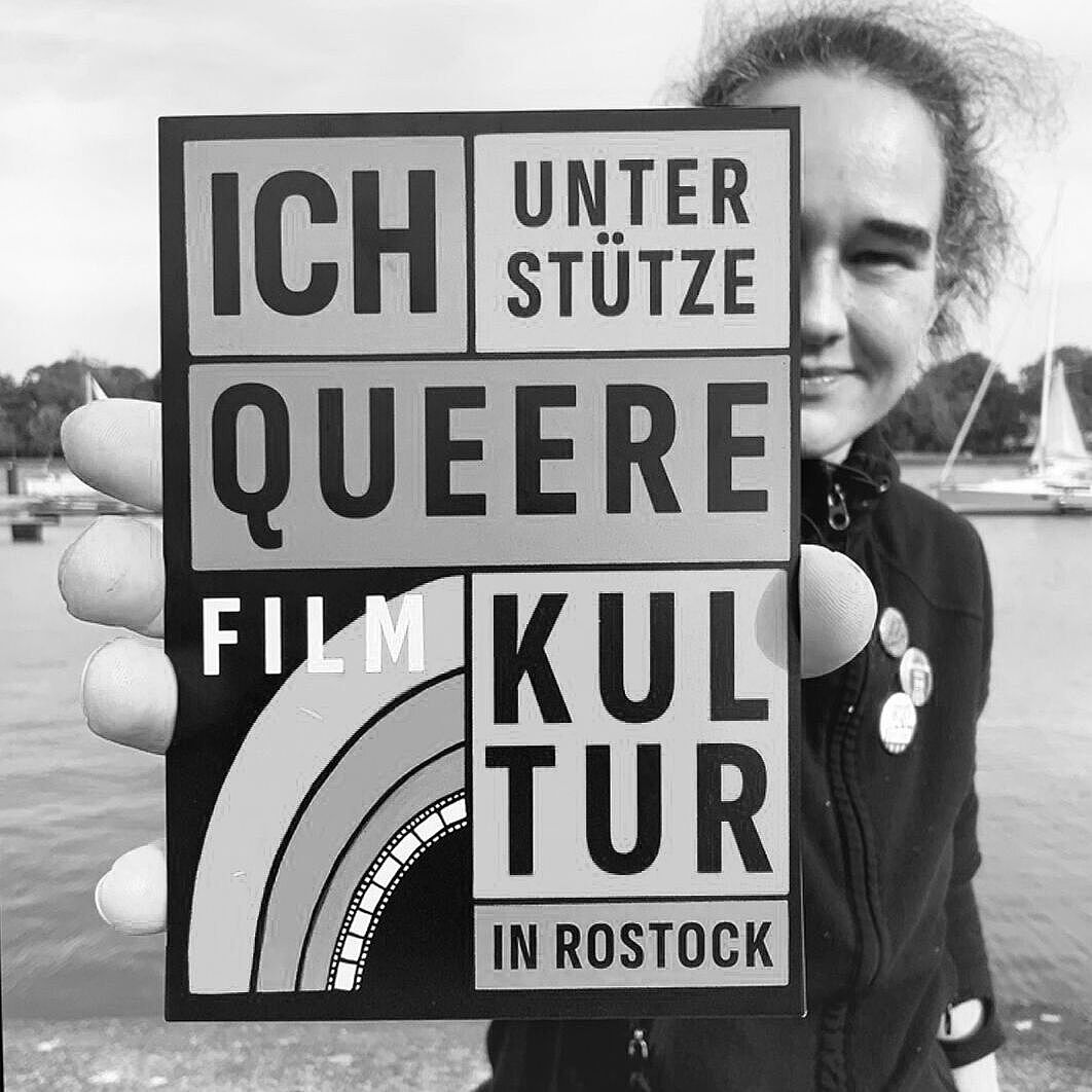 Theresa Brunk hält einen Aufkleber mit dem Text "Ich unterstütze queere Filmkultur in Rostock"