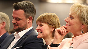 Publikum Es sind die Gesichter von drei Personen zu sehen, die schmunzeln oder lachen.