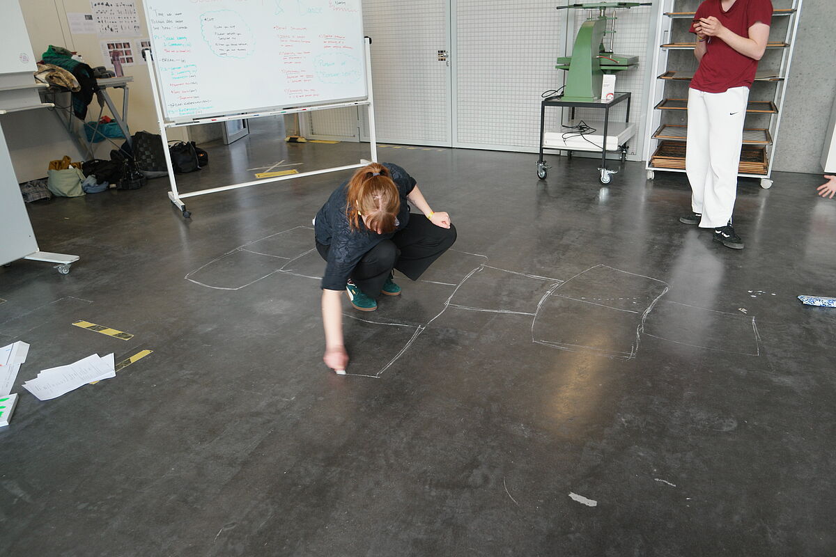 Eine Person steht in selbst gezeichneten Quadraten auf dem Boden und nimmt an einer Übung im Workshop "Social Identity and Dance" teil.