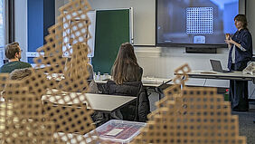 Im Vordergrund steht eine Wabenstruktur auf einem Tisch während im Hintergrund unscharf eine Studentin während der Präsentation zu sehen ist.