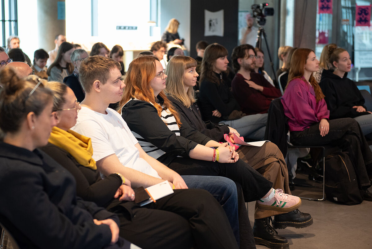 Mehrere Personen sitzen im Publikum und schauen zur Bühne. Die Aufnahme zeigt den Zuschauerbereich während der Eröffnung des reflektor – Festival der Kommunikation.