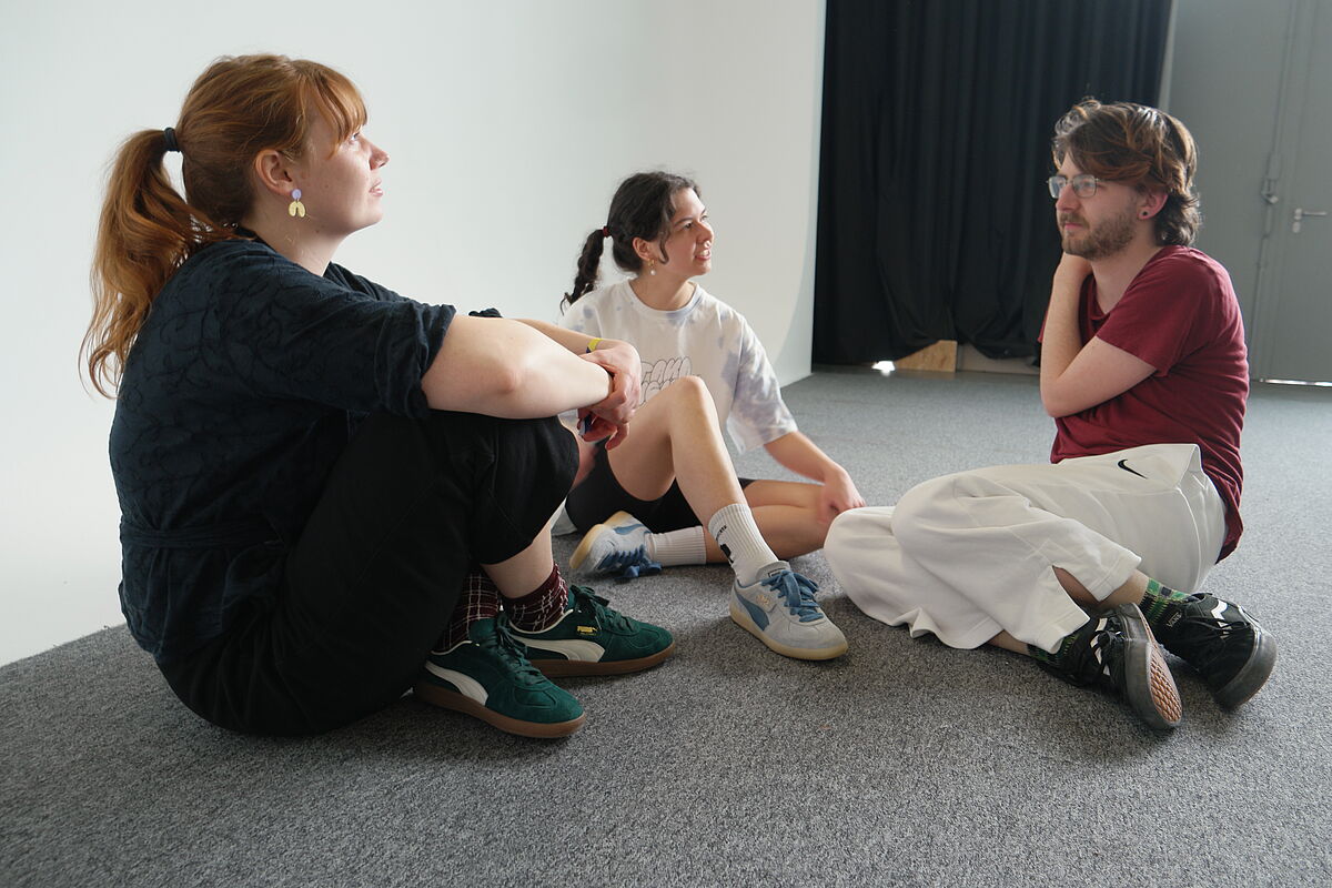 Drei Teilnehmende sitzen im Kreis und tauschen sich während des Workshops "Social Identity and Dance" über verschiedene Aspekte des Themas aus.