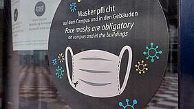 Aufkleber Aufkleber an einer Gebäudeeingangstür, der auf die Maskentragepflicht hinweist.