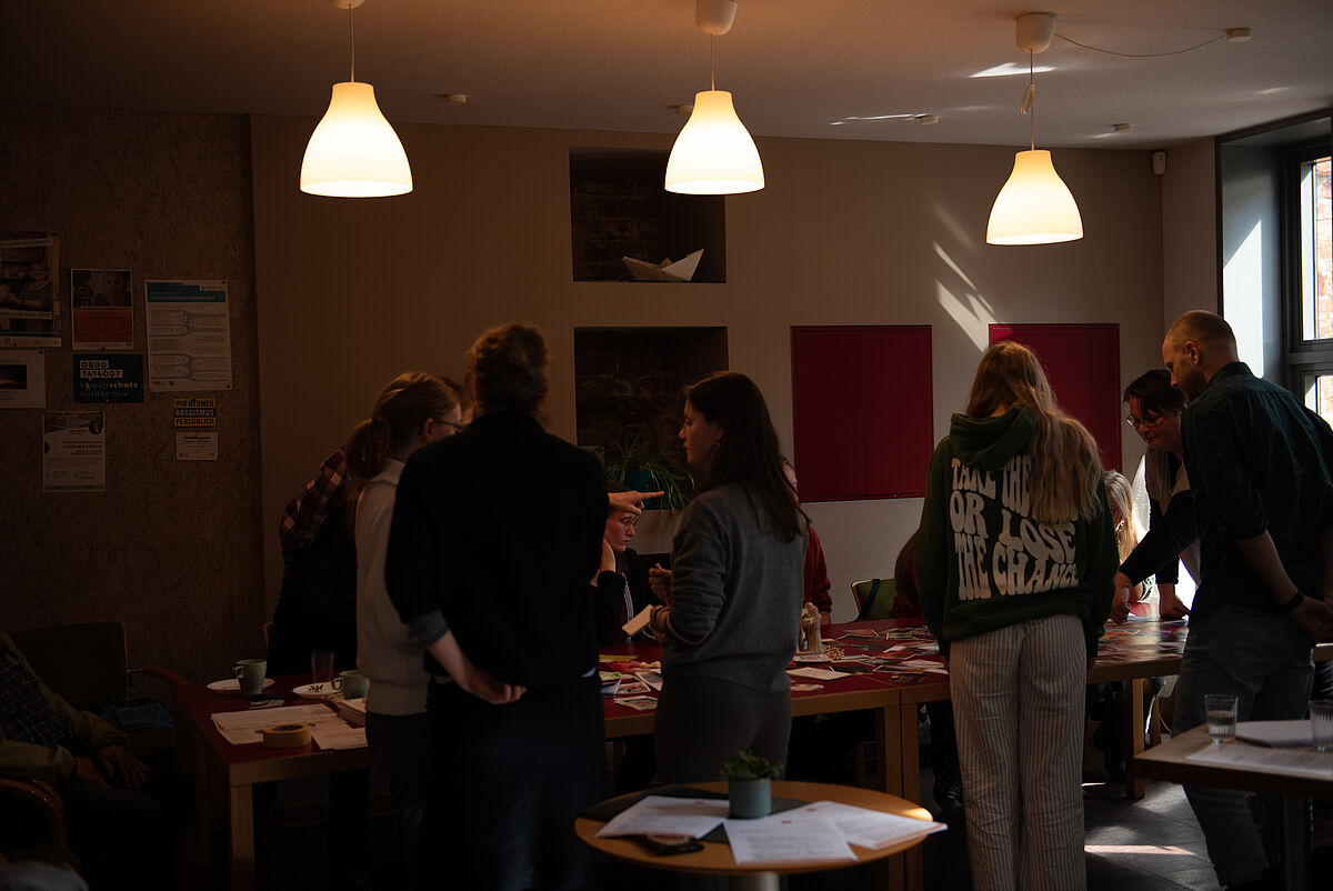 Mehrere Workshopteilnehmende stehen um einen Tisch in der Begegnungsstätte des Boot e. V. und arbeiten gemeinsam an Konzeptideen.