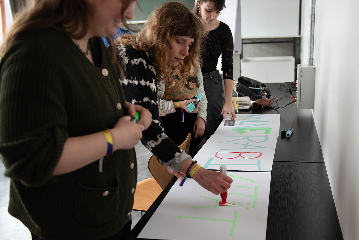 Teilnehmende arbeiten gemeinsam an einem Plakat, auf dem sie ihre Erkenntnisse und Ergebnisse aus dem Workshop zum Thema Vulnerabilität festhalten.