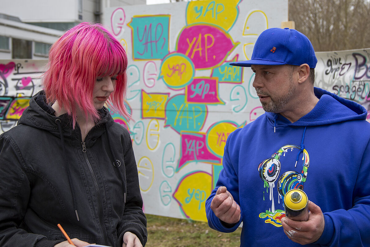 Scraby, der Graffiti-Künstler, unterhält sich mit einer Teilnehmerin während des Workshops.