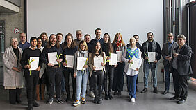 Gruppenbild, auf dem im Vordergrund nebeneinander die ausgezeichneten Studierenden mit Urkunden in den Händen zu sehen sind.