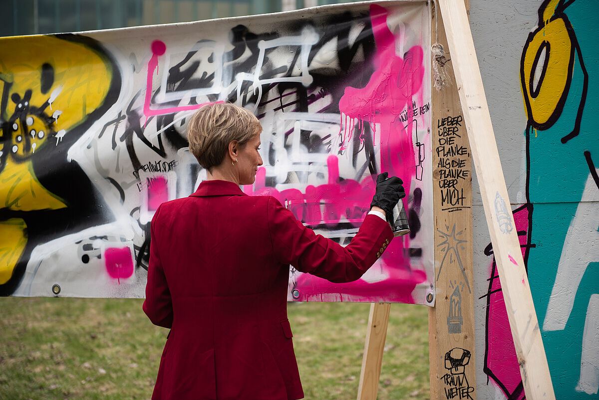 Eine Professorin sprüht Farbe auf ein Banner während des Graffiti-Workshops zum Thema Inklusion.