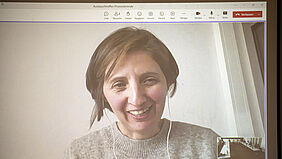 Die Person ist auf einem Livebild zu sehen. In der rechten unteren Ecke ist ein kleines Bild aus dem Raum mit allen Teilnehmenden zu erkennen.