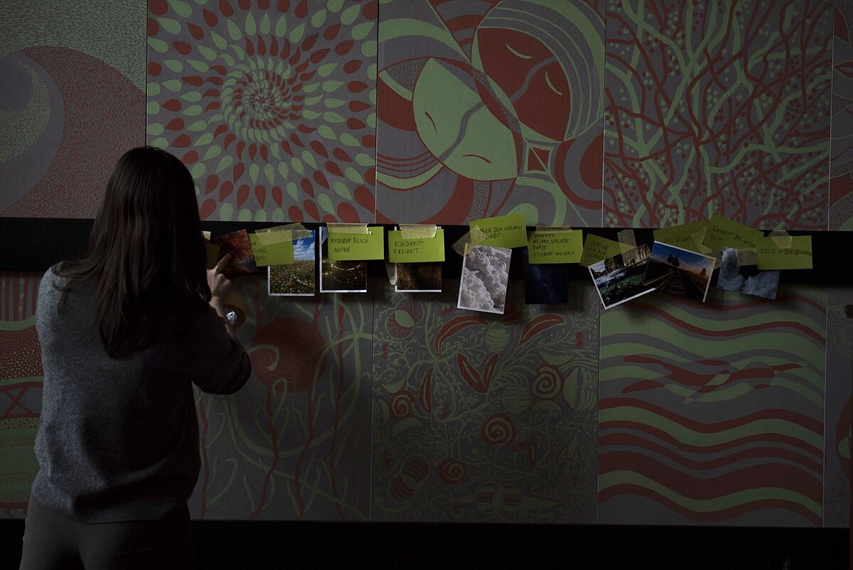 Eine Teilnehmerin des Workshops "Die B(o)otschaft – Partizipation und Engagement" hängt einen Zettel mit Ideen an eine Wand, auf der bereits weitere Ausarbeitungen zu sehen sind.