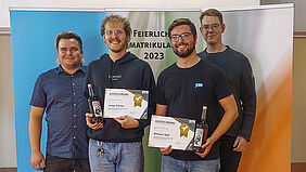 Stud. Engagement Lukas und Leif stehen gemeinsam mit zwei Ausgezeichneten, diese mit BLumen und Urkunden in der Hand, gemeinsam vor einer Bannerwand, auf der Feierliche Immatrikulation 2023 steht