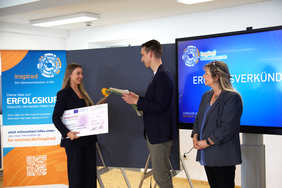 Svea Bublys, smiling, receives a prize certificate and flowers from a jury member at the award ceremony of the INSPIRED innovation competition at Wismar University of Applied Sciences.